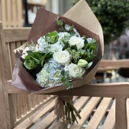Bouquet of white roses and pale blue hydrangeas wrapped in brown paper