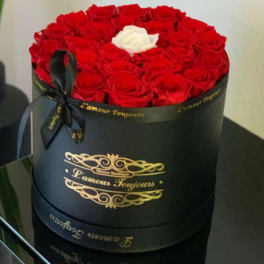 Round box of red roses with one white rose on top and a black ribbon