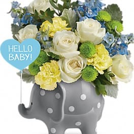 Bouquet of white roses, yellow carnations, and blue flowers in a gray elephant planter with a "Hello Baby" sign.