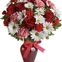 Red roses and white daisies in a red vase with a polka-dot ribbon