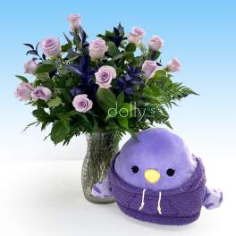 Lavender roses in a glass vase beside a purple plush bird