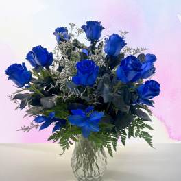 Blue roses arranged in a clear glass vase with greenery