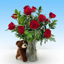 Red roses in a glass vase with a teddy bear beside it