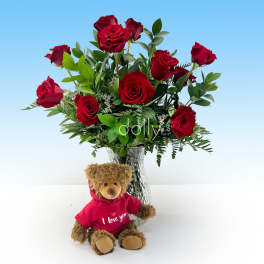 Red roses in a glass vase with a teddy bear in a red shirt