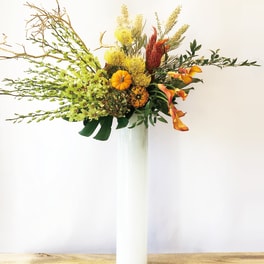 Tall autumn floral arrangement in a white vase with orange and yellow blooms