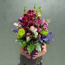 Mixed bouquet with burgundy orchids, pink blooms, and a purple vase