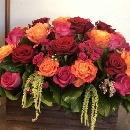 Low rectangular arrangement of red, orange, and hot pink roses in a wooden box