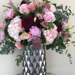 Tall arrangement of pink and burgundy flowers in a silver textured vase