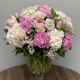 Large pink and white arrangement of peonies, roses, tulips and hydrangeas in a clear glass vase