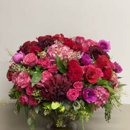 Low, lush arrangement of red and pink flowers in a clear glass pedestal bowl