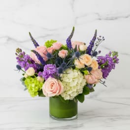 Bouquet of pink and cream roses with purple flowers in a green vase