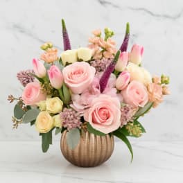 Pink and cream floral arrangement in a ribbed gold vase
