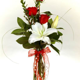 Red roses and a white lily in a clear glass vase with a red ribbon