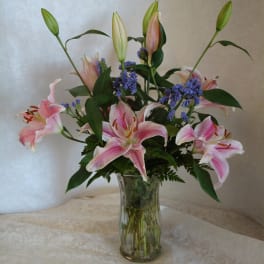 Pink lilies and purple filler flowers in a clear glass vase