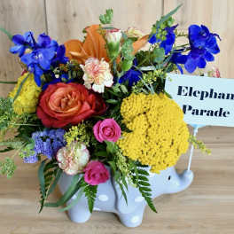 Colorful flower arrangement in a white elephant container with a sign reading Elephant Parade
