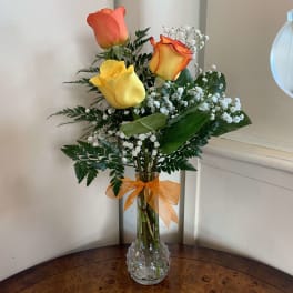 Three roses in a clear vase with baby's breath and an orange ribbon