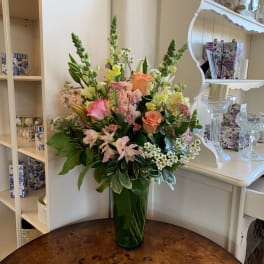Mixed bouquet in a tall glass vase with pink, peach, and yellow flowers