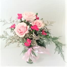 Pink roses and hot pink blooms in a clear vase with a pink ribbon