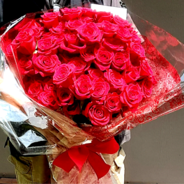 Large bouquet of bright red roses wrapped in shiny paper with a red ribbon