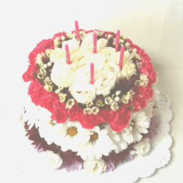 Round floral cake with white roses, daisies, and pink candles
