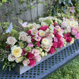 Long floral centerpiece of pink and cream roses with butterfly accents