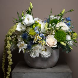 Mixed bouquet of white, blue, and green flowers in a gray vase