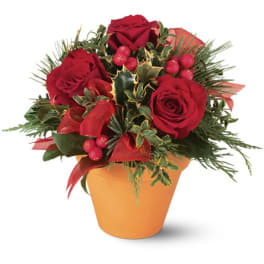 Red roses arranged in an orange pot with berries and evergreen accents