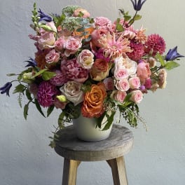 Large mixed bouquet of pink, peach, and purple flowers in a white vase