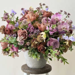 A mixed bouquet of pink, lavender, and peach flowers in a gray vase.