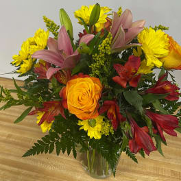 Mixed bouquet of yellow daisies, roses, lilies, and red alstroemeria in a glass vase