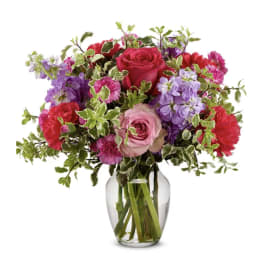 Mixed pink, purple, and red flowers in a clear glass vase