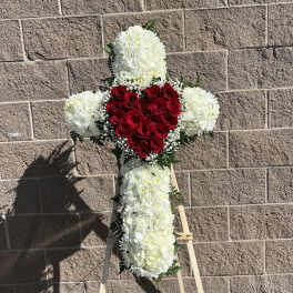 Cross-shaped floral tribute with red roses and white flowers on an easel