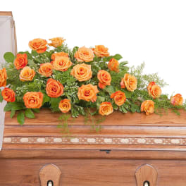 Long spray of orange roses arranged on top of a wooden casket