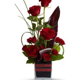 Red roses arranged in a black square vase with dark foliage accents
