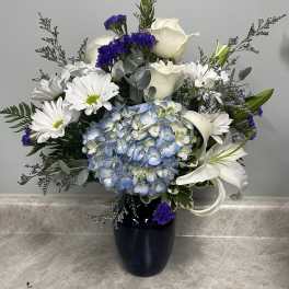 Blue hydrangea bouquet with white roses, lilies, and daisies in a dark vase