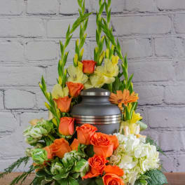 Orange roses and pale yellow flowers arranged around a gray urn