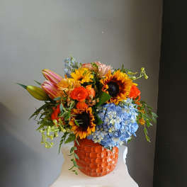 Colorful mixed bouquet in an orange textured vase with sunflowers and blue hydrangea