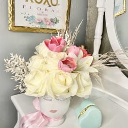 Pink and white flower arrangement in a face-shaped vase with a ribbon
