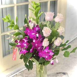 Pink roses and purple orchids in a clear glass vase