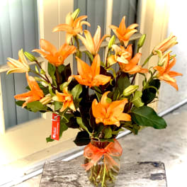 Orange lilies in a glass vase with a ribbon bow