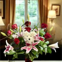 Bouquet of red roses and pink lilies in a red vase with a teddy bear center