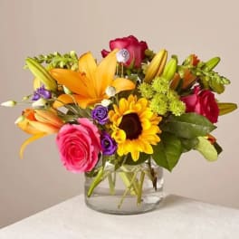 Mixed bouquet of roses, lilies, and a sunflower in a glass vase