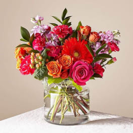 Mixed bouquet of roses, gerbera daisies, and carnations in a clear glass vase