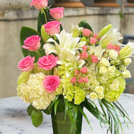 Pink roses and white lilies arranged in a tall green vase