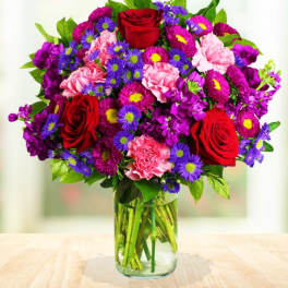 Bouquet of red roses, pink carnations, and purple daisies in a glass vase