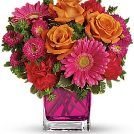 Pink and orange mixed bouquet in a magenta glass vase