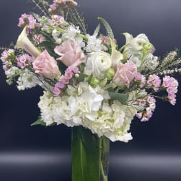 Tall vase arrangement with white hydrangeas, pink roses, calla lilies, and mixed white and pink blooms