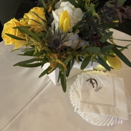 Yellow roses and white flowers arranged in a white box with napkins beside it.
