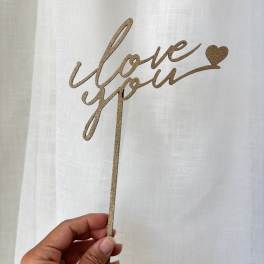 Hand holding a glittery gold "love you" cake topper