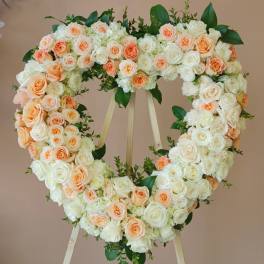 Heart-shaped floral wreath of white and peach roses on a stand